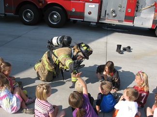 Firefighter high fiving with kids with engine in background