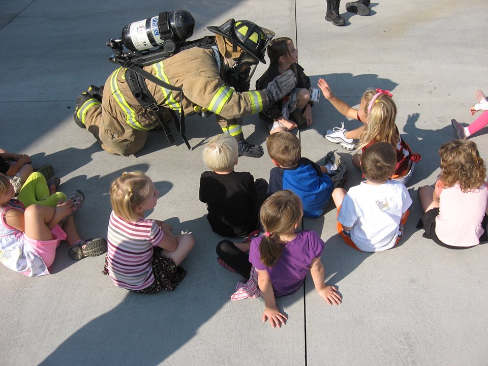 Firefighter in turnout gear giving kids high fives